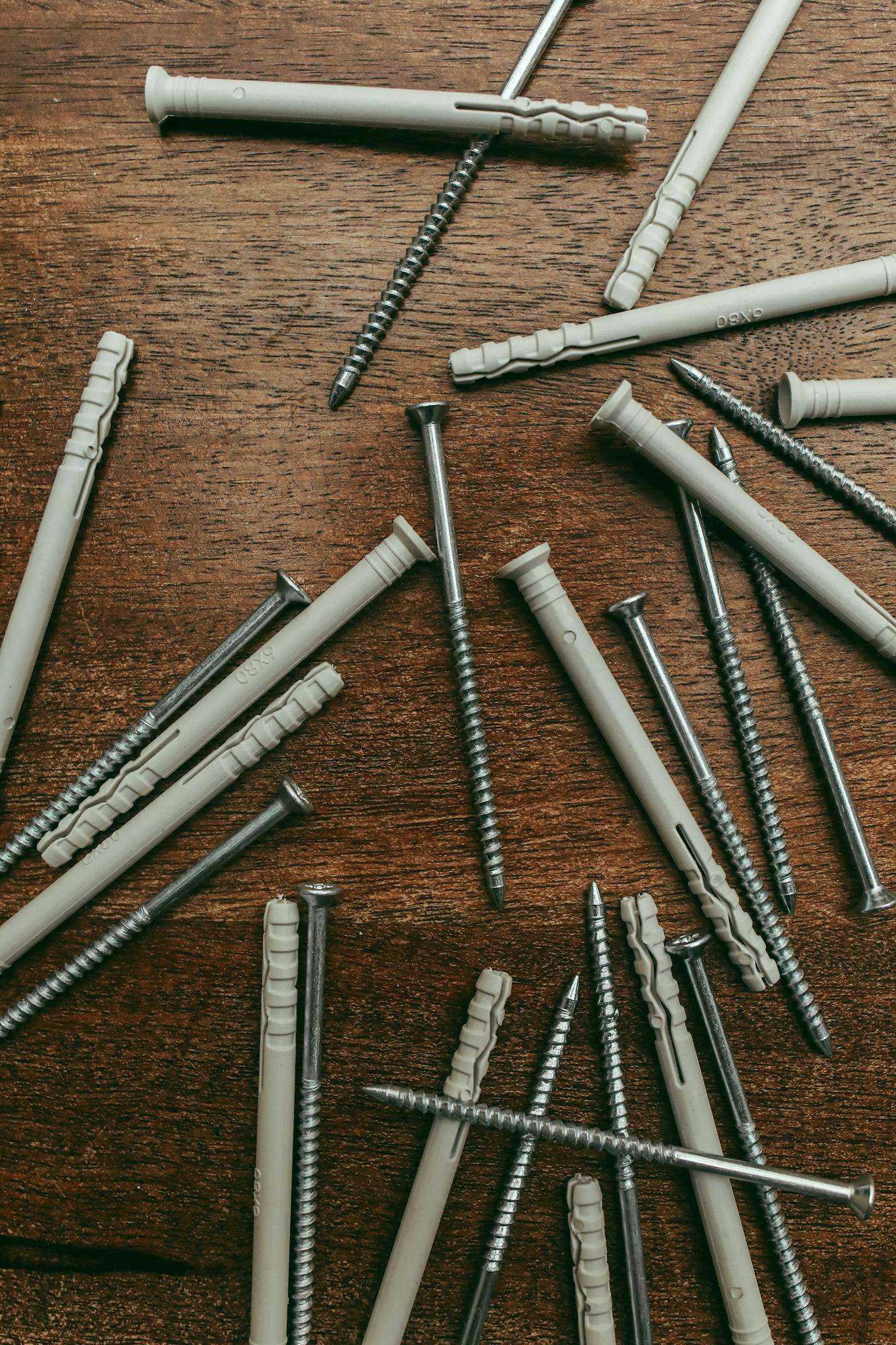 Scattered screws and nylon anchors on a wooden table, ideal for hardware and construction themes.